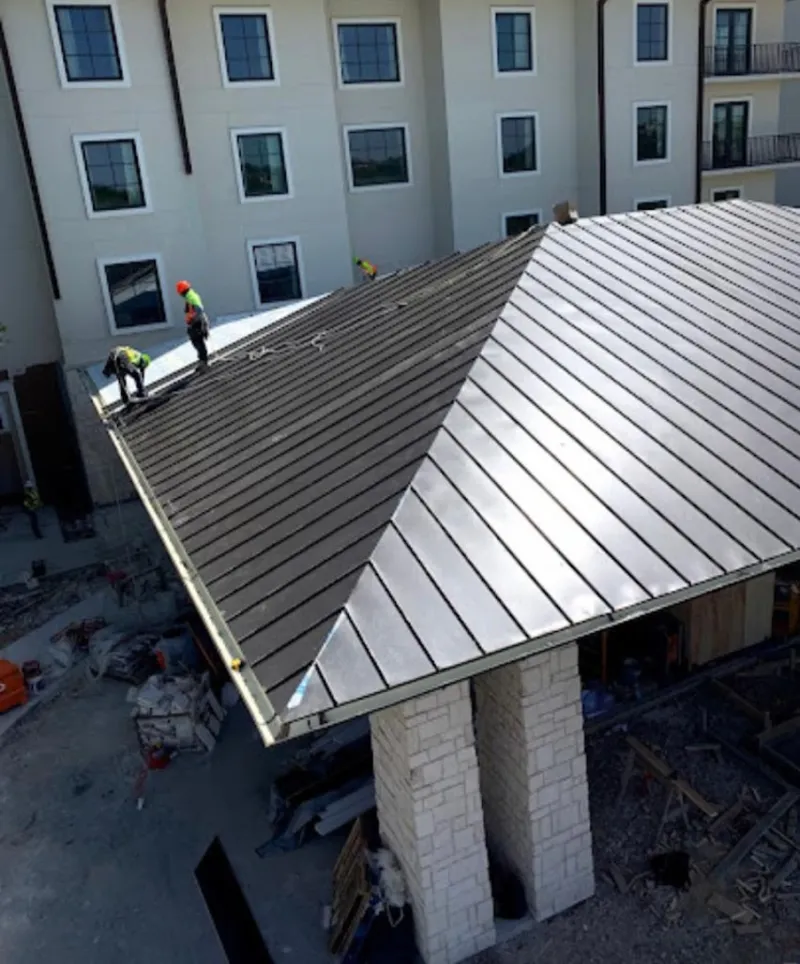 Crew installing standing seam metal roof panels on a commercial project in Giddings